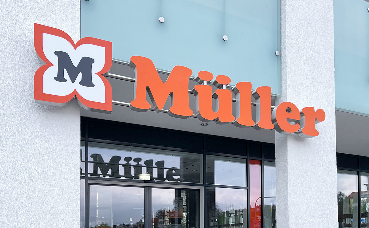 Eingang eines Müller Drogeriemarkts mit großem orangefarbenem Logo und Schriftzug an moderner weißer Fassade