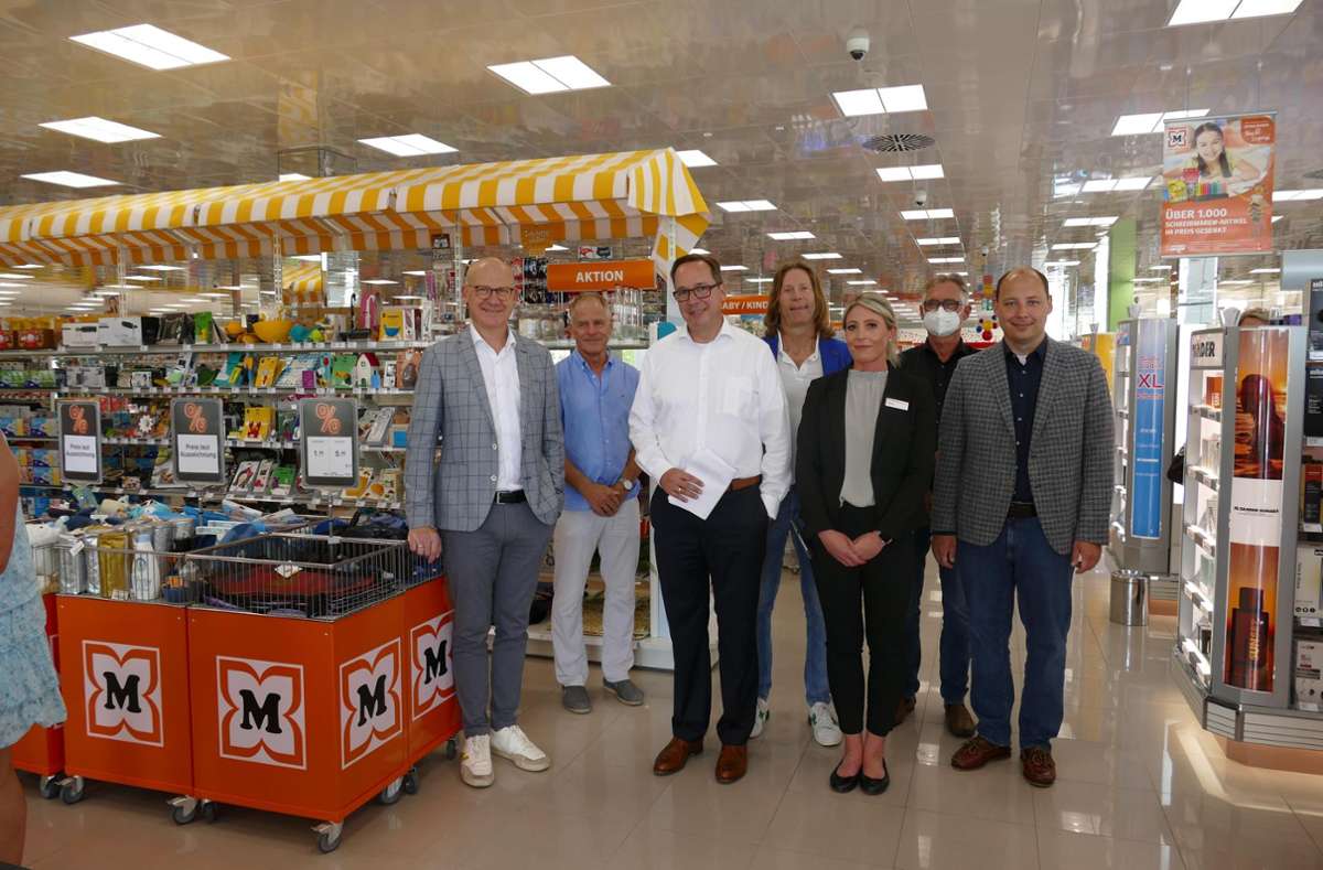 Gruppenfoto von sieben Personen in einem Möbel- und Haushaltswaren-Geschäft mit orange-weißem Marktplatzstand und Produktangeboten im Hintergrund, geeignet für SEO im Bereich Einzelhandel, Einrichtung und Unternehmertreffen.