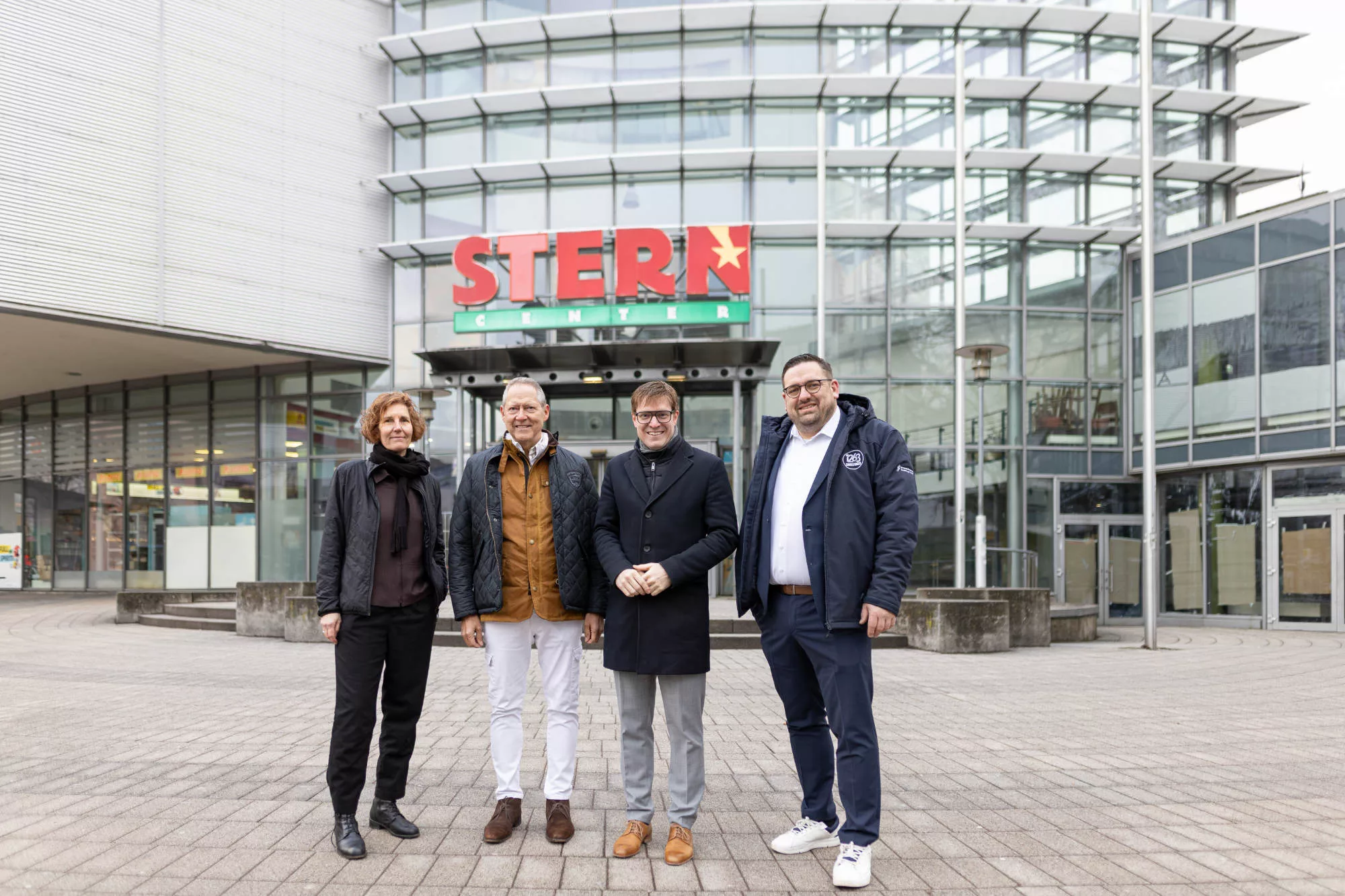 Vier Personen stehen vor dem modernen Glasgebäude des STERN Centers auf gepflastertem Platz.